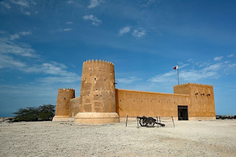 Sand-coloured Al Zubarah Fort with its corner towers under a blue sky