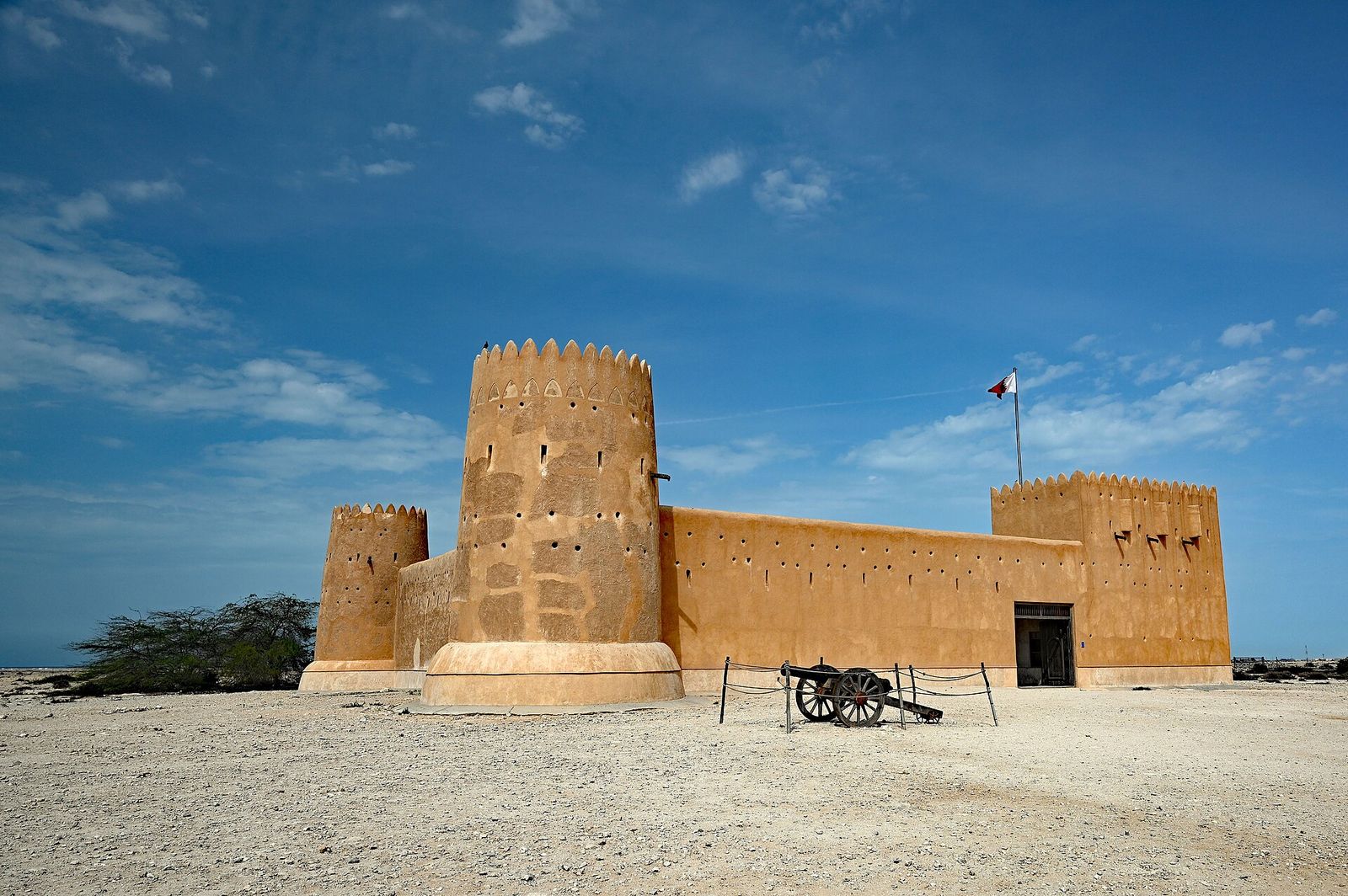 Al Zubarah Fort, a sand-coloured fort with round and rectangular corner towers, under a blue sky in north-west Qatar
