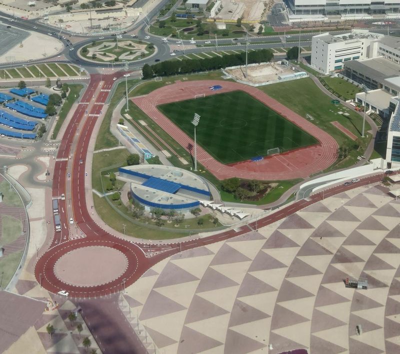 Aspire Zone from above: a training pitch and running track beside a patterned pedestrian plaza