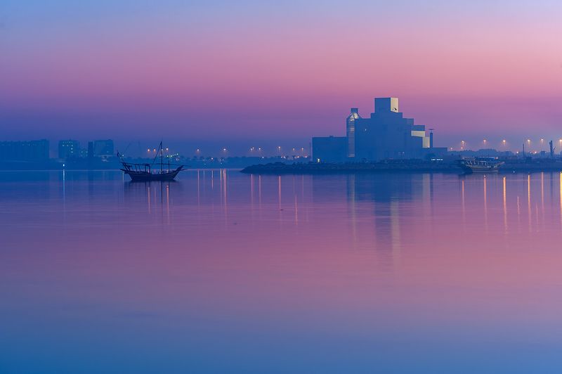 The Museum of Islamic Art silhouetted at dusk across Doha Bay, with a dhow anchored nearby