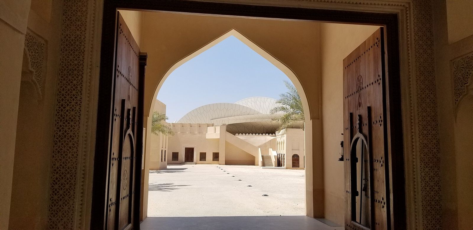 The disc-shaped roof of the National Museum of Qatar seen through a traditional arched wooden gateway