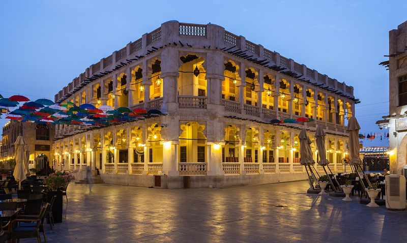 Lantern-lit arcades of a restored building in Souq Waqif at blue hour, with coloured umbrellas strung overhead